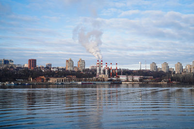 Smoke emitting from chimney by river against sky