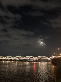 Illuminated bridge over river against sky at night