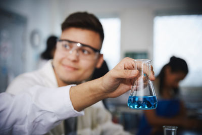 Cropped hand of male student holding solution in conical flask by friend at chemistry laboratory