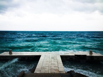 Water splashing on jetty by sea against sky