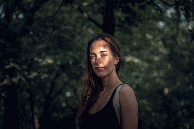 Portrait of young woman standing against trees