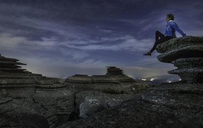 Low angle view of man on rock against sky at dusk