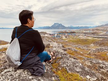 Side view of man sitting on rock at beach