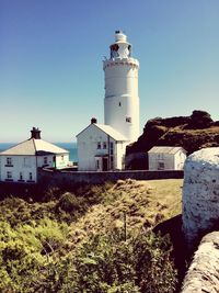 Lighthouse by building against clear blue sky