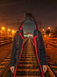 Rear view of man standing on railroad tracks at night