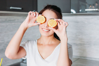Smiling woman holding orange slices against eyes at home