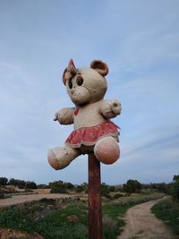 Stuffed toy on wooden post by road against sky