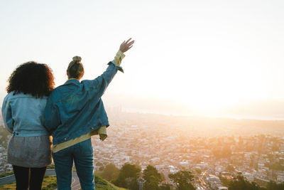 Rear view of female friends looking at cityscape against sky during sunset