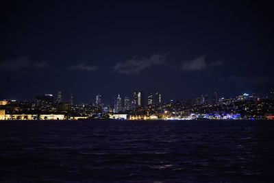 Illuminated city by sea against sky at night