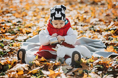 Little cute girl drinks tea from a thermos in the autumn park. cute little toddler baby with