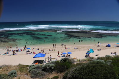 Panoramic view of people on beach against clear blue sky