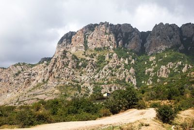 Rocky mountain landscape with winding dirt road under dramatic sky.