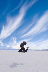 Woman jumping on salt flat against blue sky