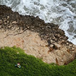 High angle view of mask on green grass over rocky coastline