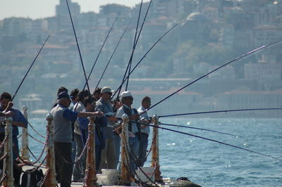 People fishing while standing on pier by sea 