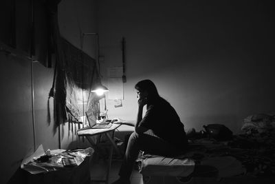 Side view of woman sitting on bed while using computer at home