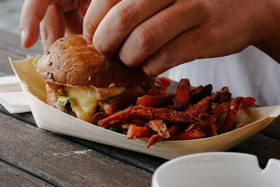 Close-up of hand holding burger in plate on table