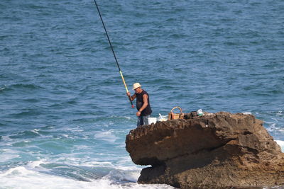 Man fishing on rock by sea