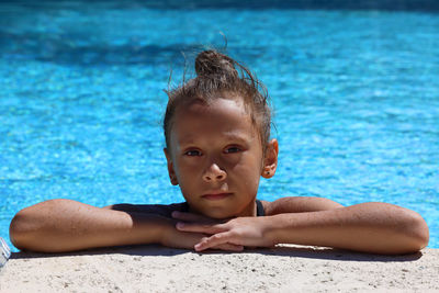 The girl in the pool leaned on her hands and looks at the camera