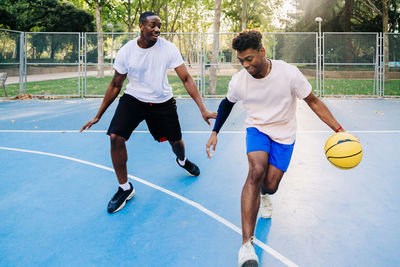 Ethnic african american friends players running together with ball while playing basketball on sports ground in sunny day