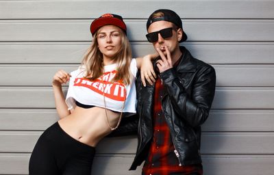 Portrait of fashionable friends standing against wall