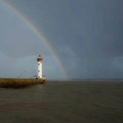 Lighthouse by sea against rainbow in sky