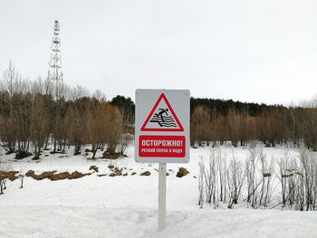 Road sign on snow covered field against sky