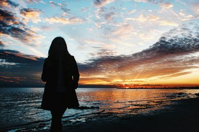 Silhouette people standing in front of sea at sunset