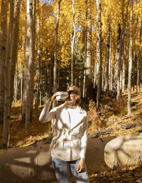 Beautiful woman drinks hot drink coffee or tea from thermos travel mug in autumn park, forest while