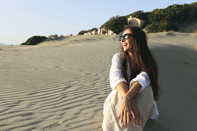 Happy young woman sitting on sand at beach, patara, turkiye