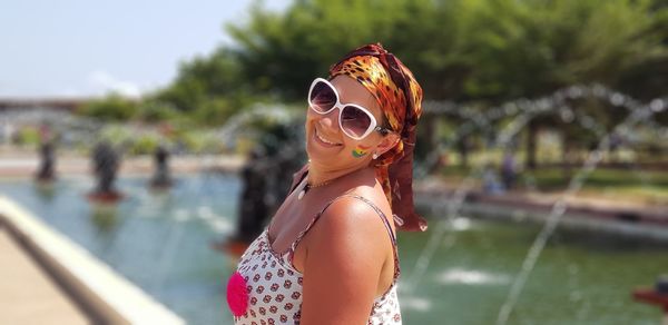 Side view portrait of smiling woman wearing sunglasses against fountain