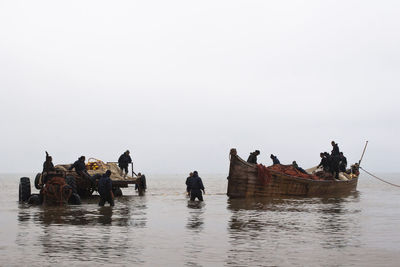 People on boats in sea against clear sky