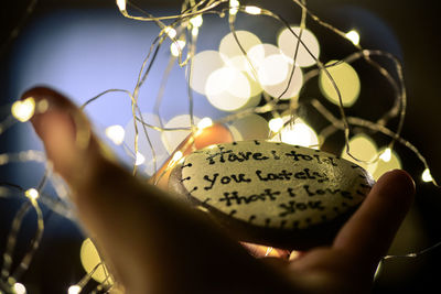 Close-up of hand holding illuminated lighting equipment hanging at night