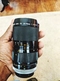 Cropped hand of man holding camera lens against carpet