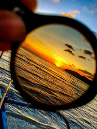 Close-up of hand against sky during sunset