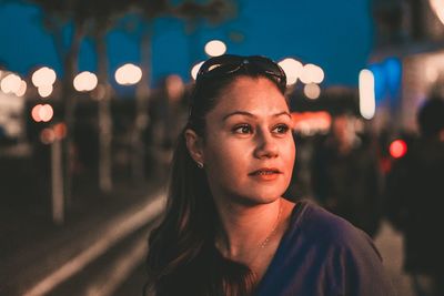 Close-up of woman looking away while standing in city at night