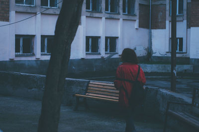 Rear view of woman sitting on bench against building