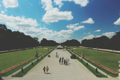 People walking on footpath amidst garden at nymphenburg palace against sky