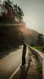 Rear view of man walking on road against sky during sunset