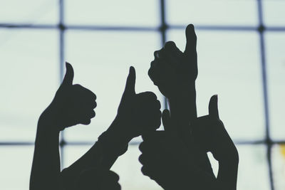 Close-up of silhouette hands showing thumbs up against window