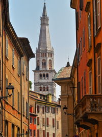 Modena tower bell named ghirlandina between buildings against clear sky