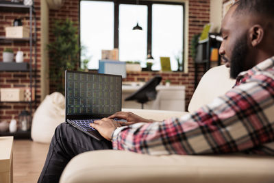 Side view of man using laptop while sitting on sofa at cafe