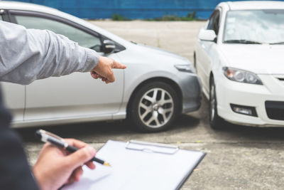 Cropped image of man showing damaged car to insurance agent on road