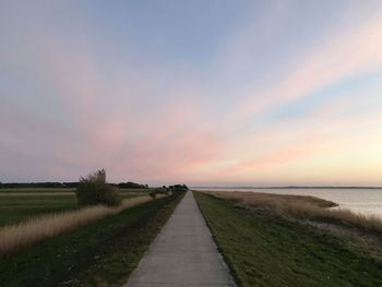 Empty road amidst field against sky during sunset