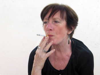 Portrait of woman smoking cigarette against wall
