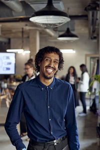 Portrait of happy businessman standing with laptop at creative office