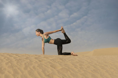 Woman with arms raised on desert against sky