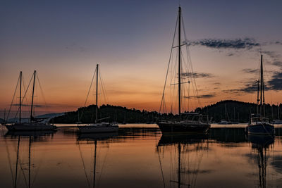 Sailboats moored at harbor against sky during sunset