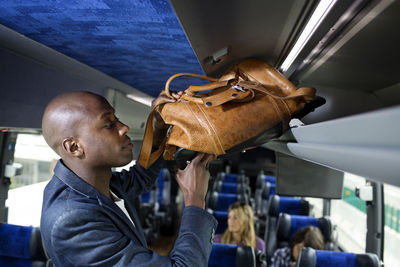 Man putting bag in luggage rack in bus