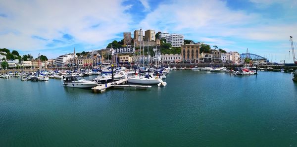 Sailboats moored in harbor against sky in city